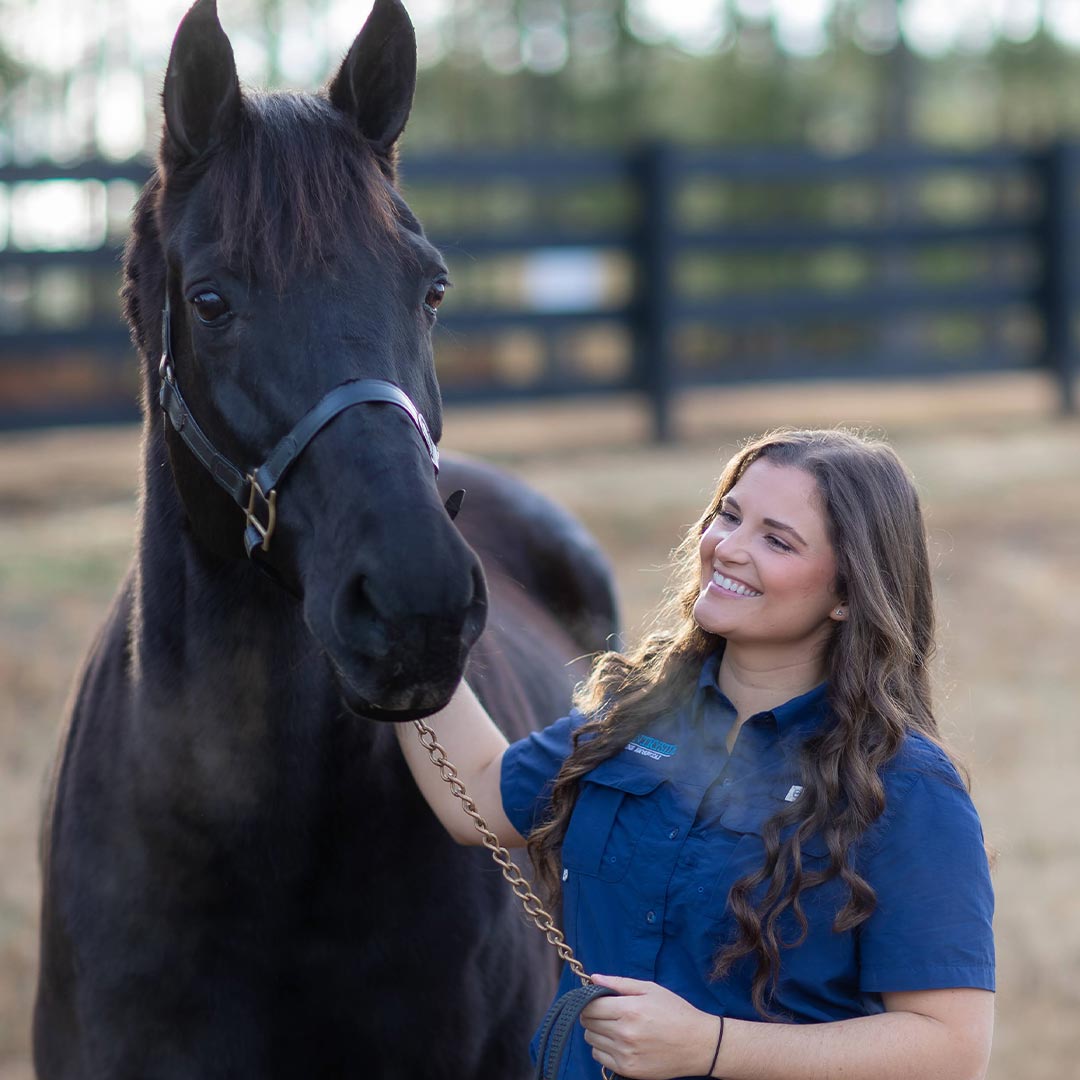 Female Veterinarian Smiling And Petting Horse Outside In Enclosed Field