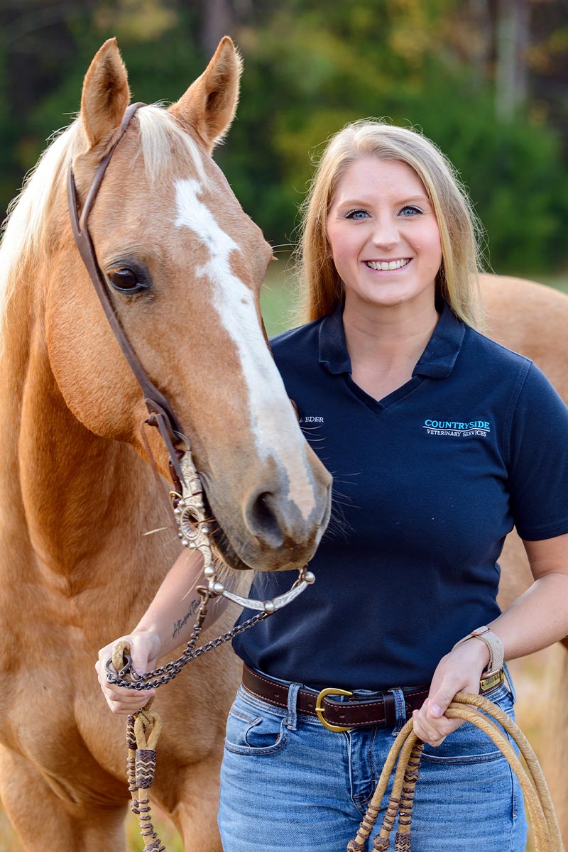 blonde female veterinarian smiling while posing next to brown and white horse