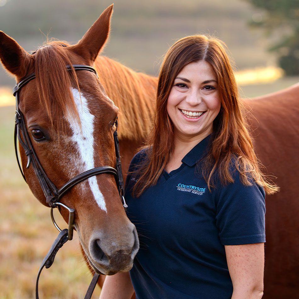 female veterinarian smiling and posing with brown horse outdoors