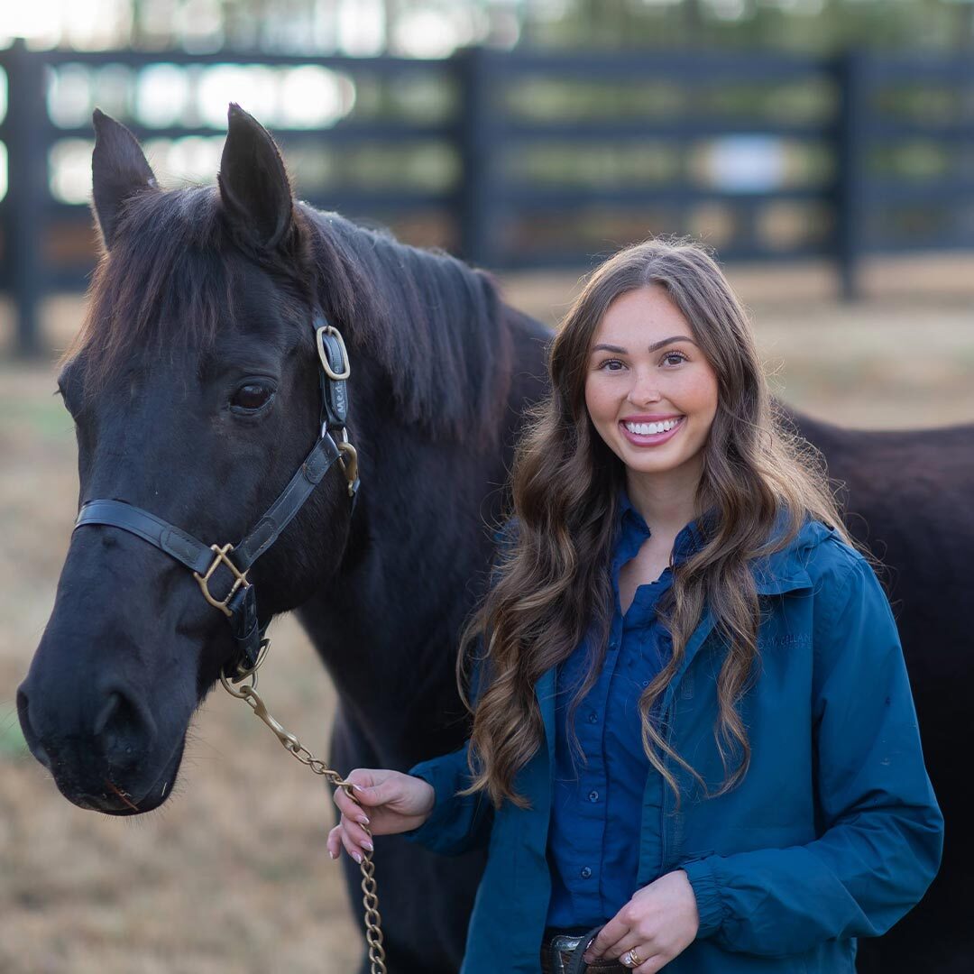 female veterinarian smiling and posing with brown horse outside